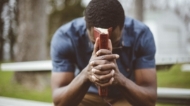 A young African-American male sitting with closed eyes with the Bible in his hands